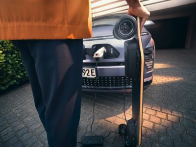 De V2L laadpoort aan de buitenkant van de Hyundai KONA Electric laadt een elektrisch skateboard op.