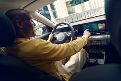 A man with a yellow shirt driving the all-new Hyundai KONA while using its touchscreen panel.