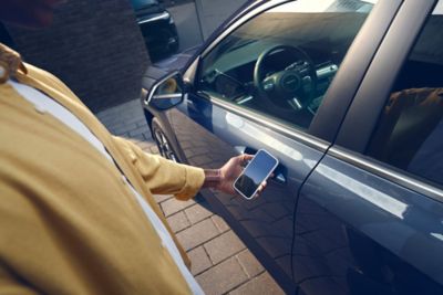 Un homme ouvrant la porte KONA Hybrid Nouvelle Génération à l’aide d’un smartphone.