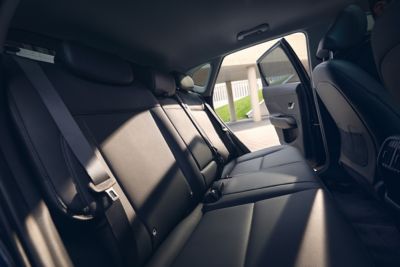 A woman sitting on the back seat of Hyundai KONA showing her smartphone to a friend outside. 