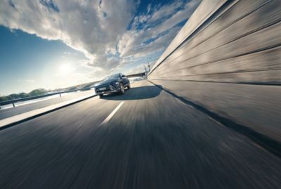 The all-new Hyundai KONA driving over a bridge in the sunshine.