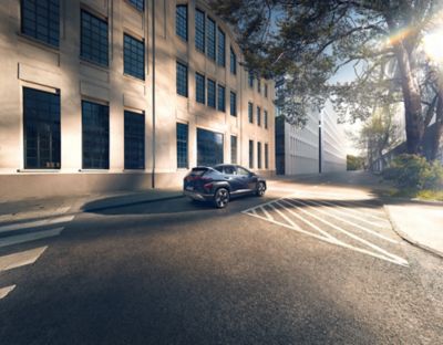 A woman crosses the street with a green Hyundai KONA is parked on the other side. 