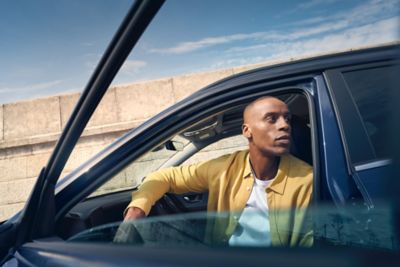 A man leaning on the front of the Hyundai KONA Electric with a city skyline in the back.