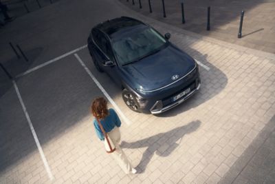 A woman walking next to the all-new Hyundai KONA in blue. 	