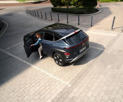 A woman exiting the all-new Hyundai KONA parked next to a building.