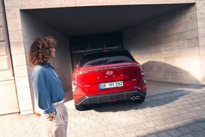 Une femme au premier plan regardant KONA Hybrid Nouvelle Génération rouge garé