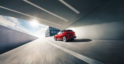 The all-new Hyundai KONA is pictured from the side driving down a city street.