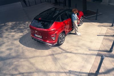 Nowy model Hyundai KONA stoi zaparkowany na leśnej drodze, a obok idzie mężczyzna.