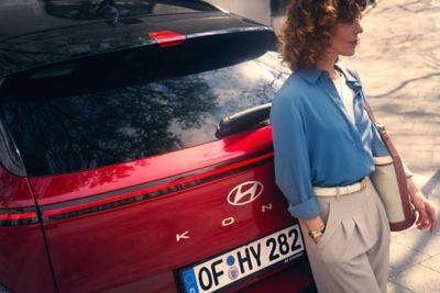 A woman with a blue shirt lands on the back of the all new Hyundai Kona in red. 