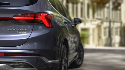 Nowy 7-miejscowy SUV Hyundai SANTA FE Hybrid zaparkowany przed domem – ujęcie z tyłu.