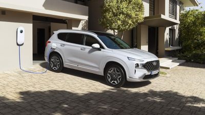 Nuevo Hyundai SANTA FE Híbrido Enchufable de 7 plazas cargándose en la entrada de una casa.