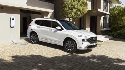 The Hyundai SANTA FE Plug-in Hybrid getting charged in front of a luxurious house.