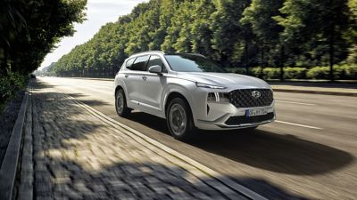 The new Hyundai Santa Fe Plug-in Hybrid 7 seat SUV parked on a city street and people leaning on it.