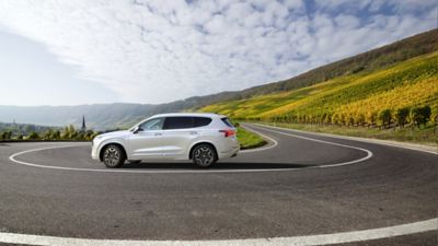 Hyundai Santa Fe Hybrid 7 seat SUV driving down the road.