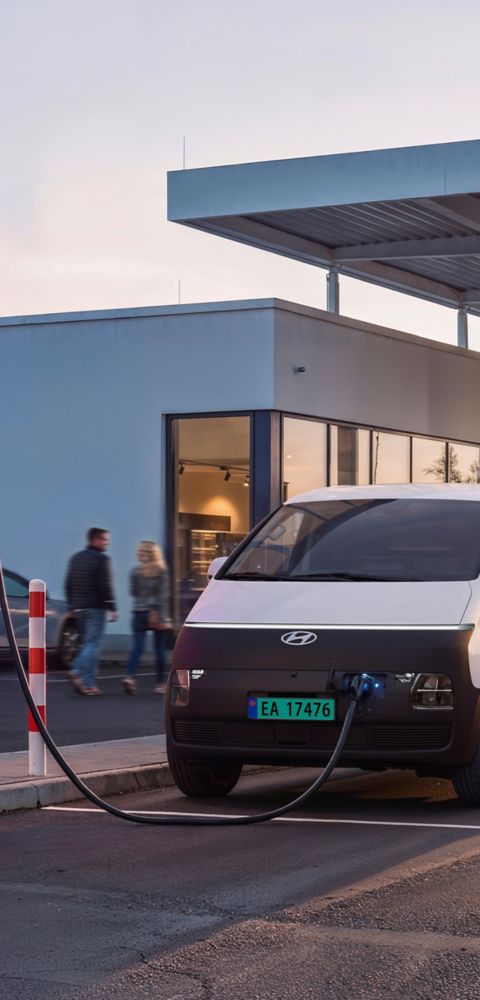Arbeider som står ved siden av en Hyundai STARIA Electric Varebil som lades på en IONITY-ladestasjon.