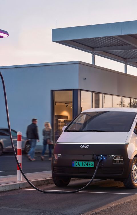 En person står ved siden av en Hyundai STARIA Electric Varebil som lades på en IONITY-ladestasjon.