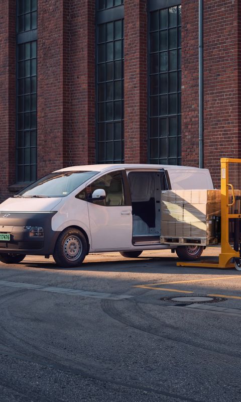 Hyundai STARIA Electric Varebil lastes med esker på paller utenfor et lager.