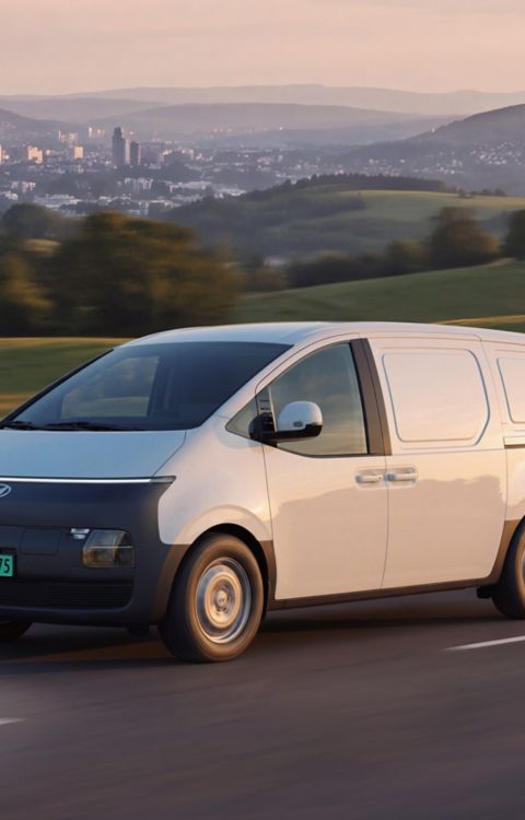 Hyundai STARIA Electric Varebil kjører på en vei i landlige omgivelser.