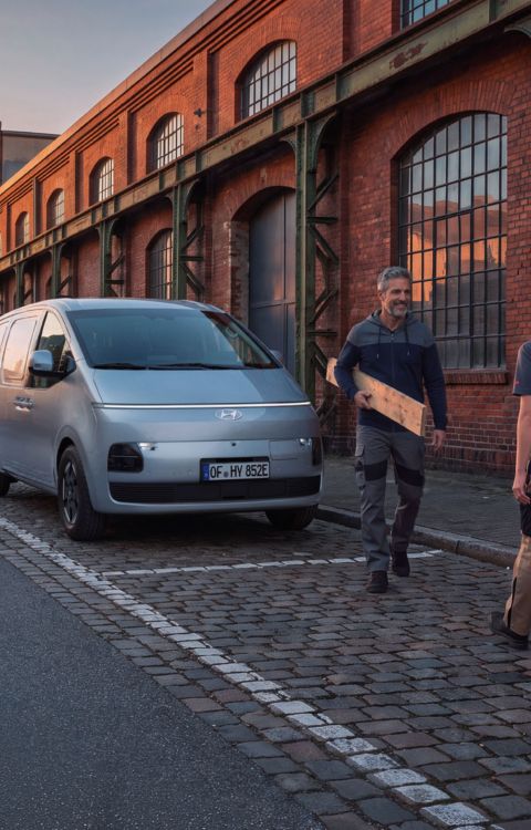To håndverkere bærer utstyr til og fra en STARIA Electric Varebil. Foto