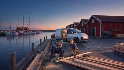 Zijaanzicht Hyundai STARIA Cargo met geopende schuifdeur, geparkeerd op een kade langs het water met op voorgrond een man en vrouw gehurkt in werkkleding.