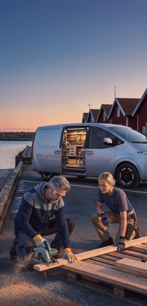 Zijaanzicht Hyundai STARIA Cargo met geopende schuifdeur, geparkeerd op een kade langs het water met op voorgrond een man en vrouw gehurkt in werkkleding.