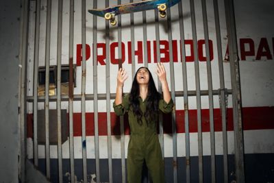 Een jonge vrouw gooit een skateboard in de lucht voor een metalen hek.