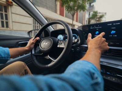 Ein Mann sitzt hinter dem Steuer eines Hyundai i20 und bedient mit einer Hand den Touchscreen.