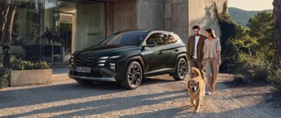 Hyundai TUCSON parkerad utanför modern villa medan ett par promenerar med en hund i kvällssol.