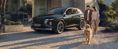 Hyundai TUCSON parkerad utanför modern villa medan ett par promenerar med en hund i kvällssol.