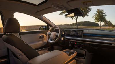 Interiör av Hyundai IONIQ 9 med vy genom vindrutan över landsväg och träd i solnedgång.
