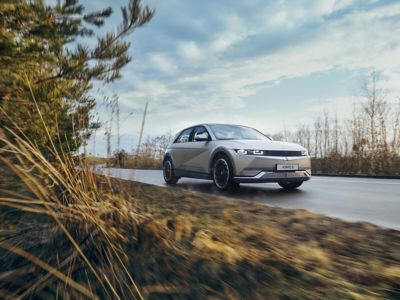 The Hyundai IONIQ 5 full electric vehicle driving down a country road.  