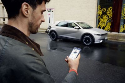 A man looking at the Bluelink on his phone with a Hyundai IONIQ 5 behind