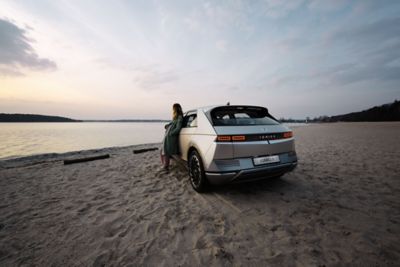 A person leaning on the IONIQ 5 in a beach scenery.