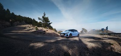 The Hyundai i20 N in performance blue driving up a hilly road.