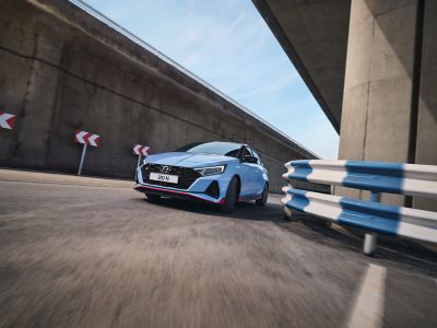 A woman sitting on the hood of the Hyundai i20 N, the driver standing in the opened door.