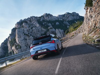 The Hyundai i20 N in performance blue rear view driving up a hilly road.