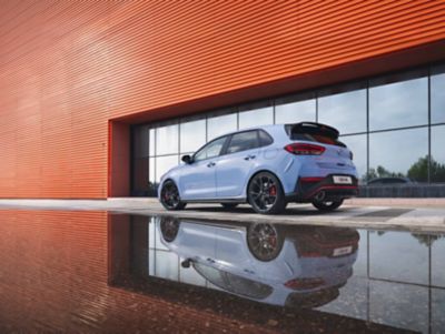 The i30 N performance hatchback from an angle, parked next to a reflective surface.