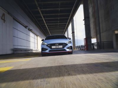 The Hyundai i30 N from the front in Performance Blue colour driving along an industrial structure