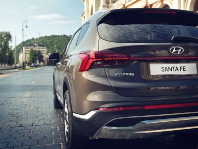 The Hyundai Santa Fe Hybrid 7 seat SUV from the rear driving down a road in the city.