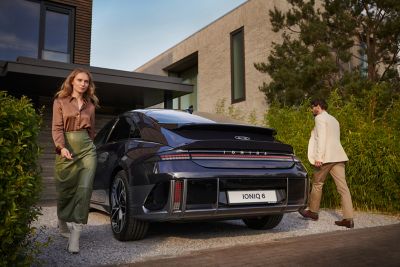 Woman and man walking around the Hyundai IONIQ 6 in a driveway.