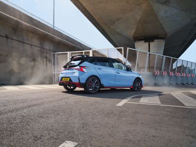 Hyundai i20 N driving rapidly through a corner seen from the back 