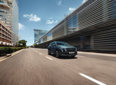 A blue Hyundai TUCSON Hybrid driving down a long, empty city street.