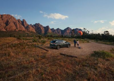 The Hyundai TUCSON Hybrid parked in a field before some mountains next to two people flying a kite.