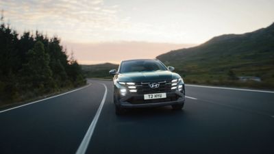 Hyundai TUCSON Plug-in Hybrid front facing driving on the road with hillside background.