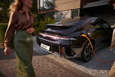 The Hyundai IONIQ 6 in charge. and a woman passing behind the vehicle.