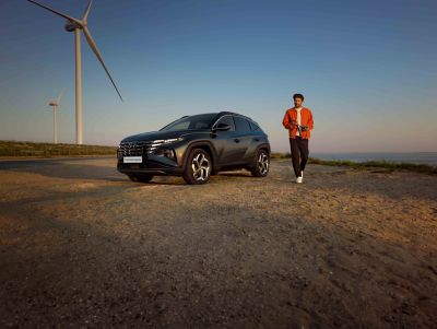 Man walking by the all-new Hyundai TUCSON Hybrid N Line between windmills.