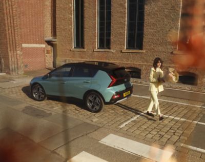 Woman in yellow walking away from the parked Hyundai BAYON compact crossover SUV.​
