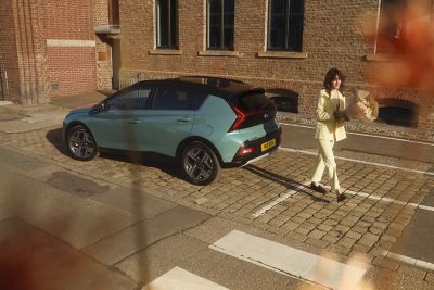 Woman in yellow walking away from the parked Hyundai BAYON compact crossover SUV.