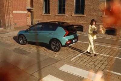 Eine Frau mit Blumenstrauß entfernt sich von einem geparkten Hyundai BAYON. 