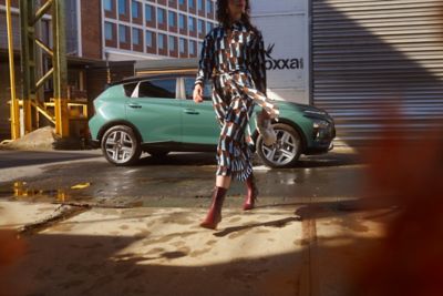 Woman crossing the street with the Hyundai BAYON compact crossover SUV parked in the background
